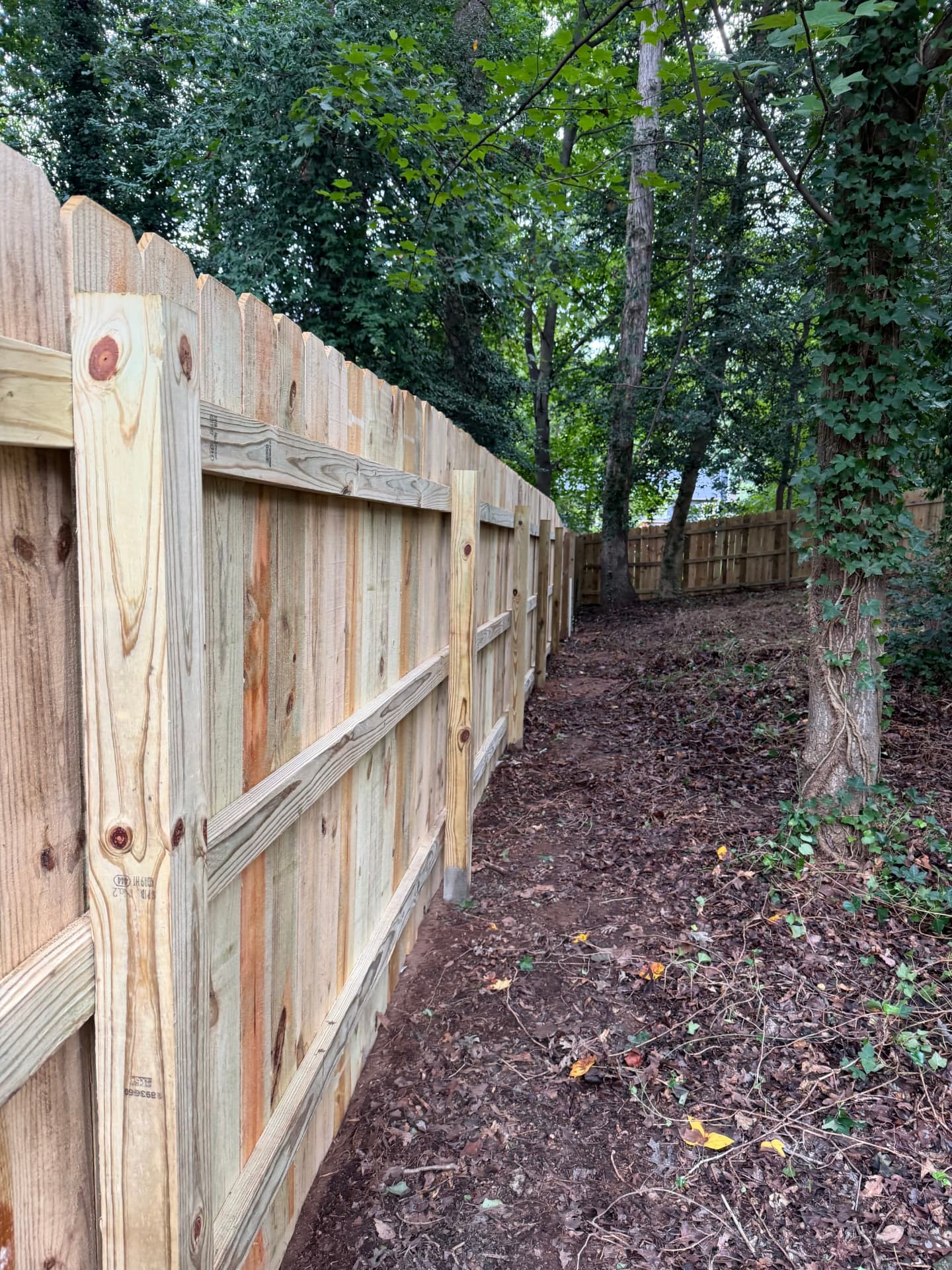 Wood privacy fence line with set posts along a wooded lot